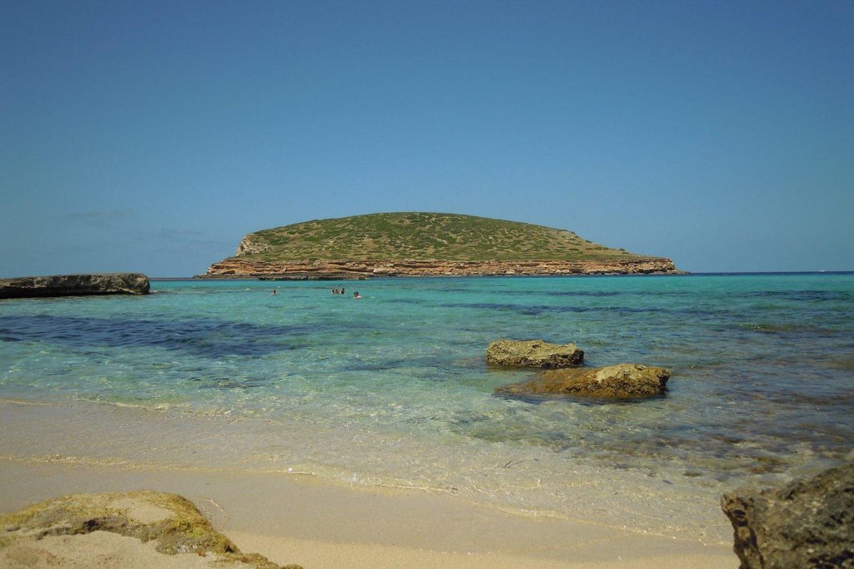 Shallow turquoise water and an islet off Cala Comte